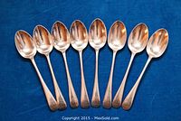 Eight sterling silver spoons laid side by side on a blue cloth
