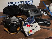 Photo showing Nikon Nikormat camera, Polaroid Captiva SLR, Minolta Freedom, and Hello Kitty Fuji camera grouped together with carrying cases