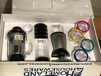 Full set showing all components including motor base, large handle cup, small cups with colored rings, and accessories arrayed inside original packaging