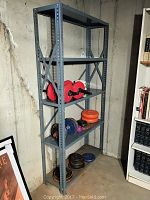 Full view of gray metal shelving unit holding assorted weight plates and dumbbells in basement corner