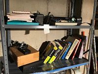 Metal garage shelving with various office and electronic items on top two shelves: loose leaf papers, Victor 1675 adding machine, electric pencil sharpener, office books, paper cutter, and protractor.