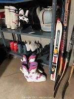 Wide shot showing two pairs of ski boots, rollerblades, ice skates, bowling balls bags and assorted hockey sticks on a storage shelf.