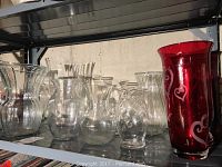 Shelf display showing a variety of clear glass vases grouped together with two red glass vases on the right side.