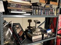 Overall view of gray metal shelving unit loaded with NES console, NES box, audio tapes and game cartridges