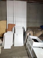 Overall view of disassembled white MDF panels, shelves, wood-tone panels, and 3-drawer cabinet unit