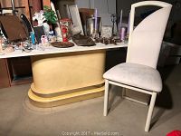 View of the white dining table with pedestal base and one matching white upholstered dining chair.