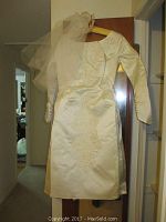 Front view of satin wedding dress hanging on wooden hanger with visible floral lace detailing and attached headpiece veil