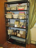 Front view of black metal shelving unit with multiple shelves, showing some storage boxes and photo frames (contents not included).