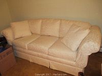 Full view of Highland House cream damask patterned sofa with three seat cushions, three pillows, arm covers, skirted bottom, and in clean condition.