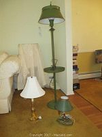 Three lamps arranged in a room: one tall green metal floor lamp with a tray, one smaller green lamp, and one brass lamp with a white shade.