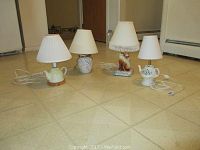 Four small table lamps on a tiled floor, showing varied ceramic bases and white lampshades.