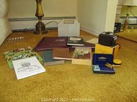 Overview of all collectibles showing books, camera box, razor in box, and other items grouped on floor