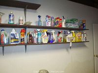 Two shelves mounted on a wall displaying various household cleaning products including sprays, liquids, powders, and containers for polished and cleaning purposes.