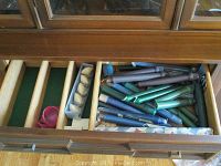 Drawer showing assorted small colored candles with holders, some wooden and carved napkin rings, and rolled dark-colored linens.