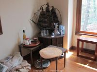 Photo including three wooden tables with finishes in a sunlit corner, metal art sailing ship sculpture on the larger table, and various dining accessories including salt and pepper shakers, wine, and glassware.