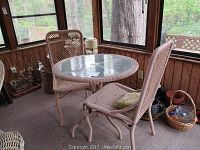 Round glass top table with two wicker patio chairs in an enclosed porch area
