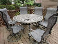 Round iron outdoor table with six matching chairs on deck, showing overall size and style.