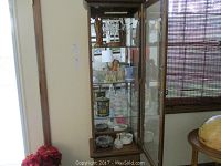 Front view of curio cabinet showing all items on three glass shelves including poinsettia sprays and ashtrays on bottom
