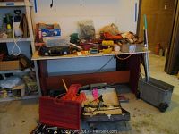 Wide shot showing wood table with assorted tools, hardware, bags and cases beneath and on top.