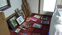 Room corner with multiple framed artworks, magazines, sheet music, wood pieces, and a flag displayed on the floor.