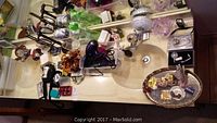 Tabletop with displayed jewelry including necklaces, rings, various bottles, hair dryer, curling iron, and a lamp.