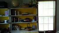 Wide view of yellow wall bookshelf showing globe, books, woven baskets, and faux flower arrangement on multiple shelves.