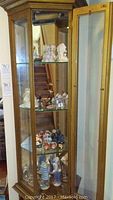 Glass-front brass curio cabinet showing shelves of porcelain figurines