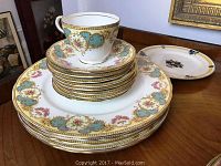 A stack of Aynsley bone china plates and saucers with a single cup on top, showing the detailed turquoise, gold and floral pattern.