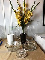 Full view of glassware lot including clear and black tinted vases, bowls, and decorative flower arrangement.