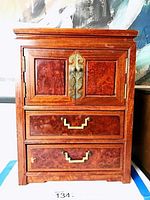 Closed handcrafted Asian wooden jewelry box with brass hardware, showing two doors on top and two drawers below.
