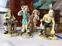 Four hand painted bisque figurines on display with varying poses and detailed painted features including a seated peasant and standing drinking men.