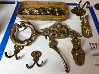 Photo showing a collection of solid brass decorative hardware including hooks, knobs, and knockers, some in a wicker tray.
