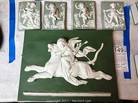 Top-down photo showing all five plaques, one large with angel on tiger and four smaller putti plaques.