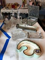 Overview of lot items including crystal cruet bottles, salt and pepper shakers, ashtrays, art glass box, and hand-painted pottery bowl on table.
