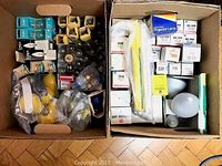 Photo showing two boxes filled with various vintage light bulbs and lamps, some in original cardboard packaging and plastic bags.