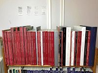 Shelf of more than 40 Christie's auction catalogs in red and white and some blue covers, arranged upright.