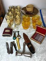 Full lot overview showing glasses, dessert bowls, flask, bottle openers, appetizer forks, baskets and ornaments on white embroidered tablecloth.