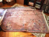 Full view of peach colored floral wool area rug with scrolled sides and blue geometric border lying on wood floor.