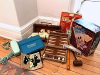 Photo of vintage kids roller skates box, board games, rotary phone, and music items arranged on wooden floor