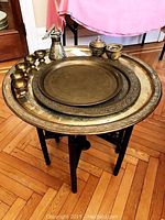 Large wooden folding tray table holding three nested brass trays and a brass tea set with teapot, bowls, and cups.