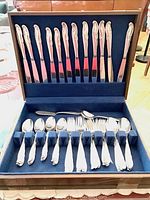 Opened wooden tarnish resistant box with blue velvet interior showing 12 knives set in upper section and variety of forks and spoons in lower section organized in compartments.