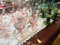 Collection of pink and green stemware glasses arranged on a lace tablecloth, showing variations in size and color.