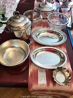 Full view of all silver plated serveware including ice bucket, platters, pot, candy dish, covered dish with Pyrex insert, and two crystal bowls.