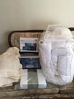 Overview of all bedding items stacked on a floral sofa, showing the duvet, knit blanket, and sealed sheet sets.