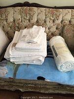 Stack of new white PC brand towels with ribbed texture on a vintage floral sofa, including bath and hand towels, and a rolled Home Styles twin fleece blanket.