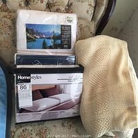 Photo showing two twin sheet sets in original packaging and a folded beige and white striped flannel blanket on floral couch.