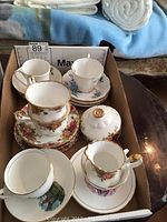 Three Royal Albert tea cups and matching saucers in floral patterns with creamer and covered sugar bowl arranged in a box.