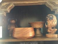 Group photo of one carved wooden bear, two wooden bowls, and one carved wooden owl all on wooden shelf