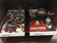 Two trays filled with various decorative glass, ceramic, and lacquer items, including rose-themed pieces and apple stir sticks.