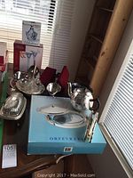 Collection of silver plated and crystal serving items on tabletop, including teapot, condiment caddy, covered dish, and boxed silverware.